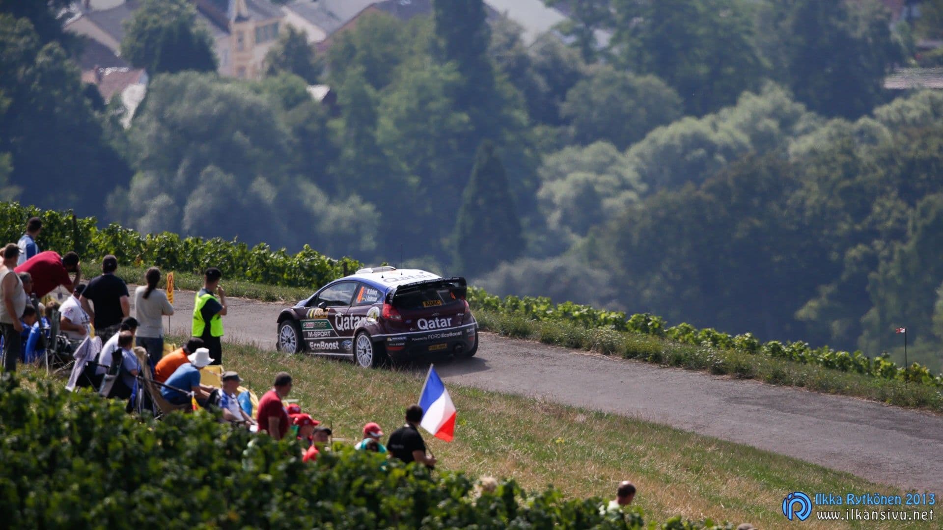 Ralliauto ajaa soratiellä rinteeseen kokoontuneiden katsojien ohi