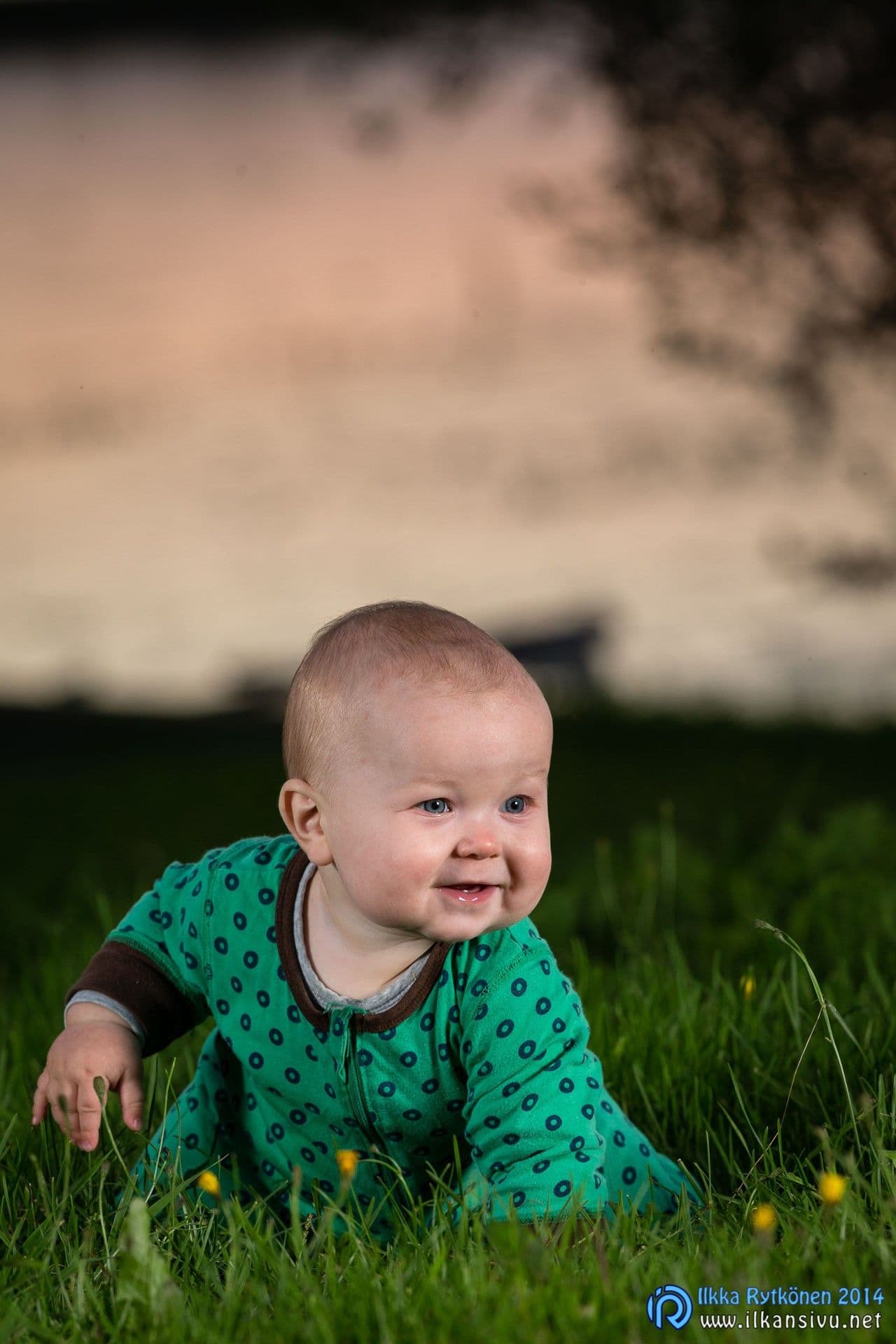 A baby in green crawls on the grass
