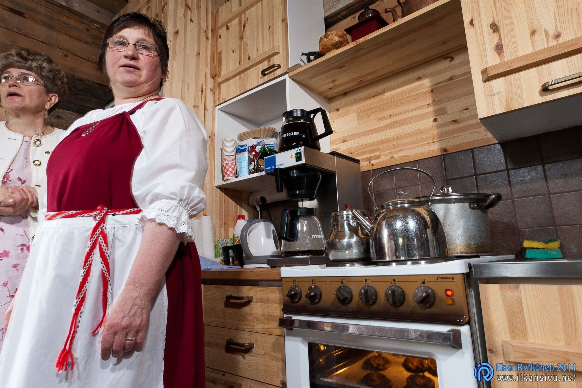 Kaksi naista seisoo keittiössä kahvinkeittimen ja uunissa paistuvien piirakoiden vieressä