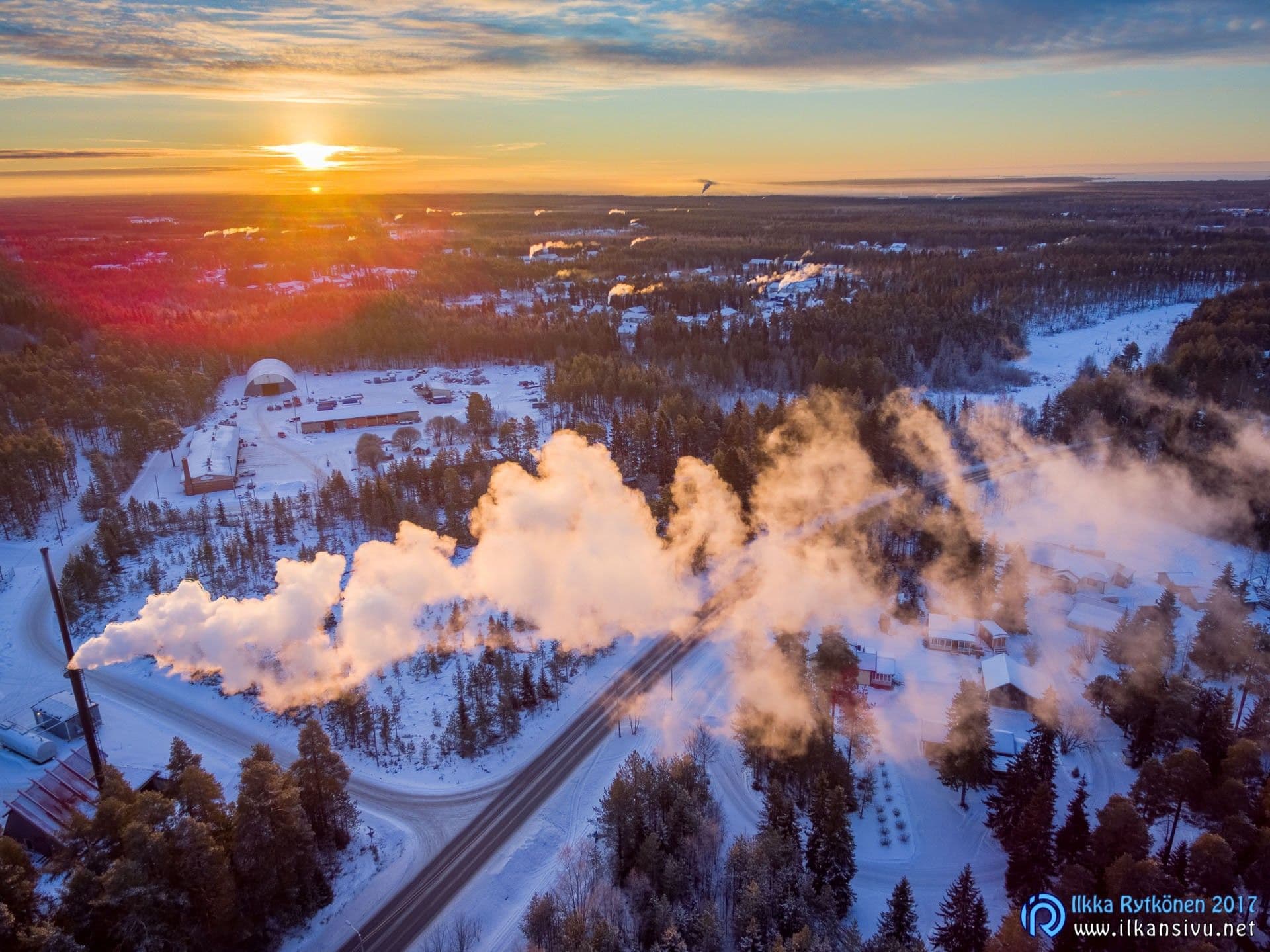 Aerial view of a snowy landscape and steam clouds in low sunlight
