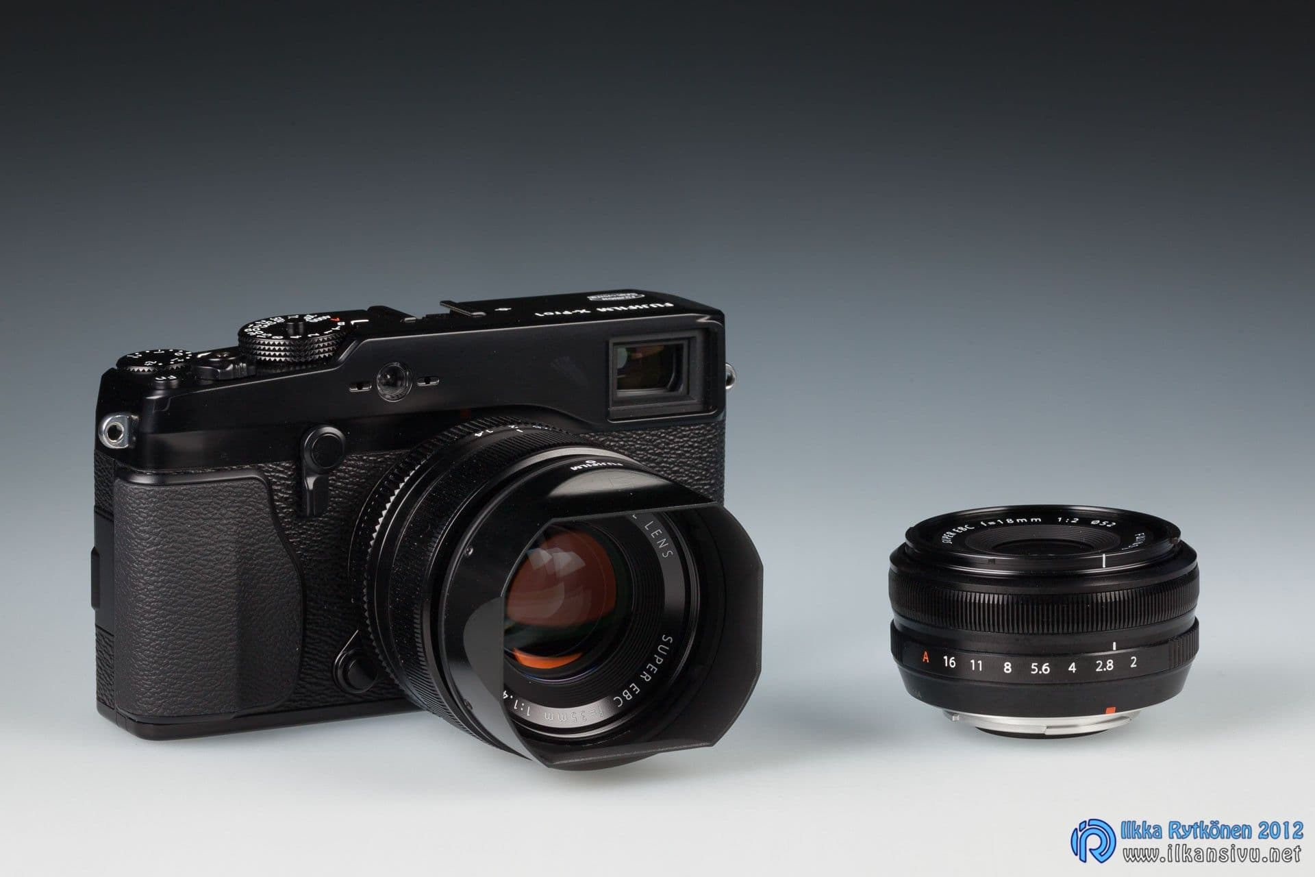 Fujifilm X-Pro1 -kamera ja kaksi objektiivia tummalla liukuväritaustalla