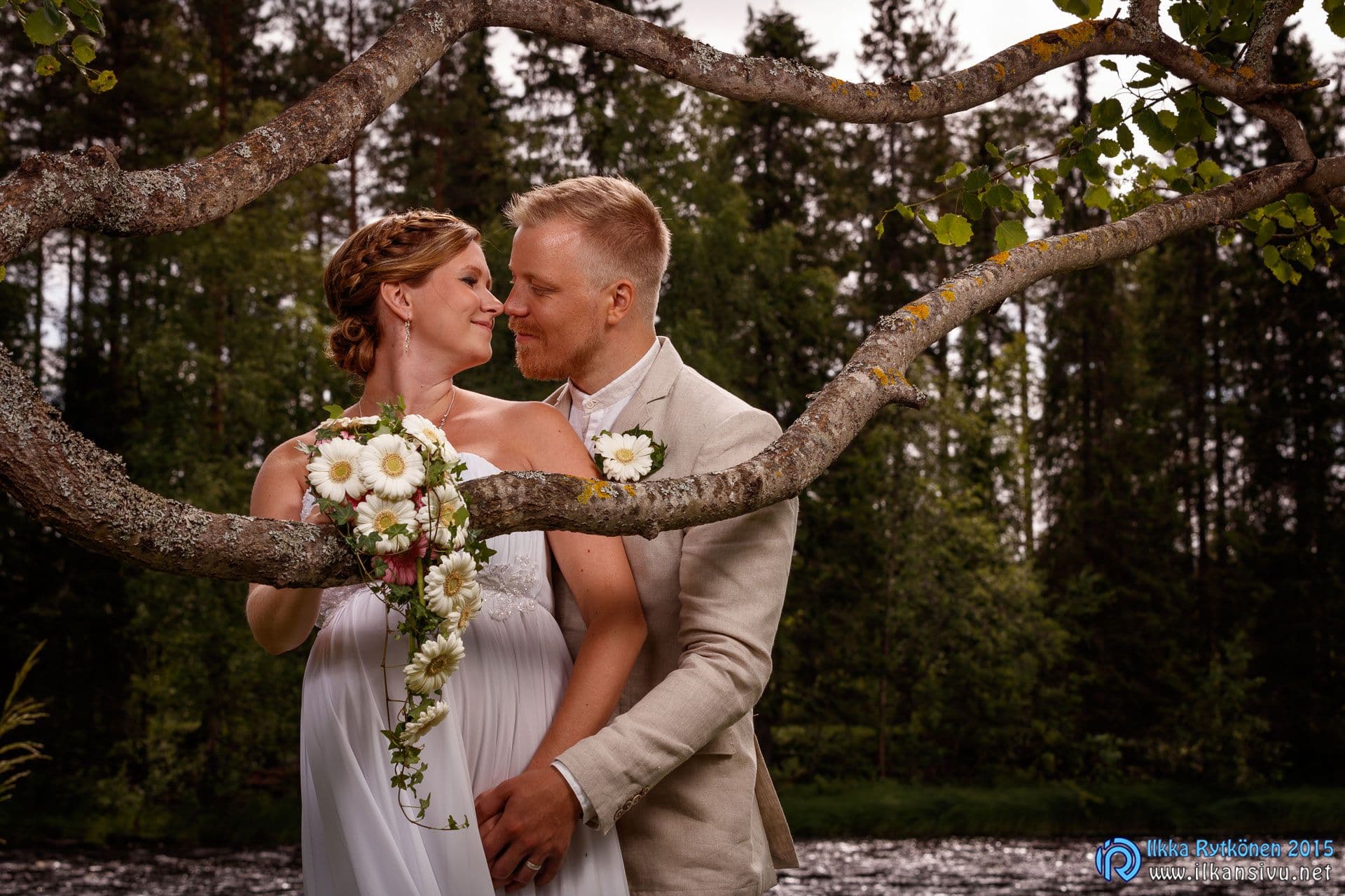 A wedding couple embracing in a forest beneath a branch