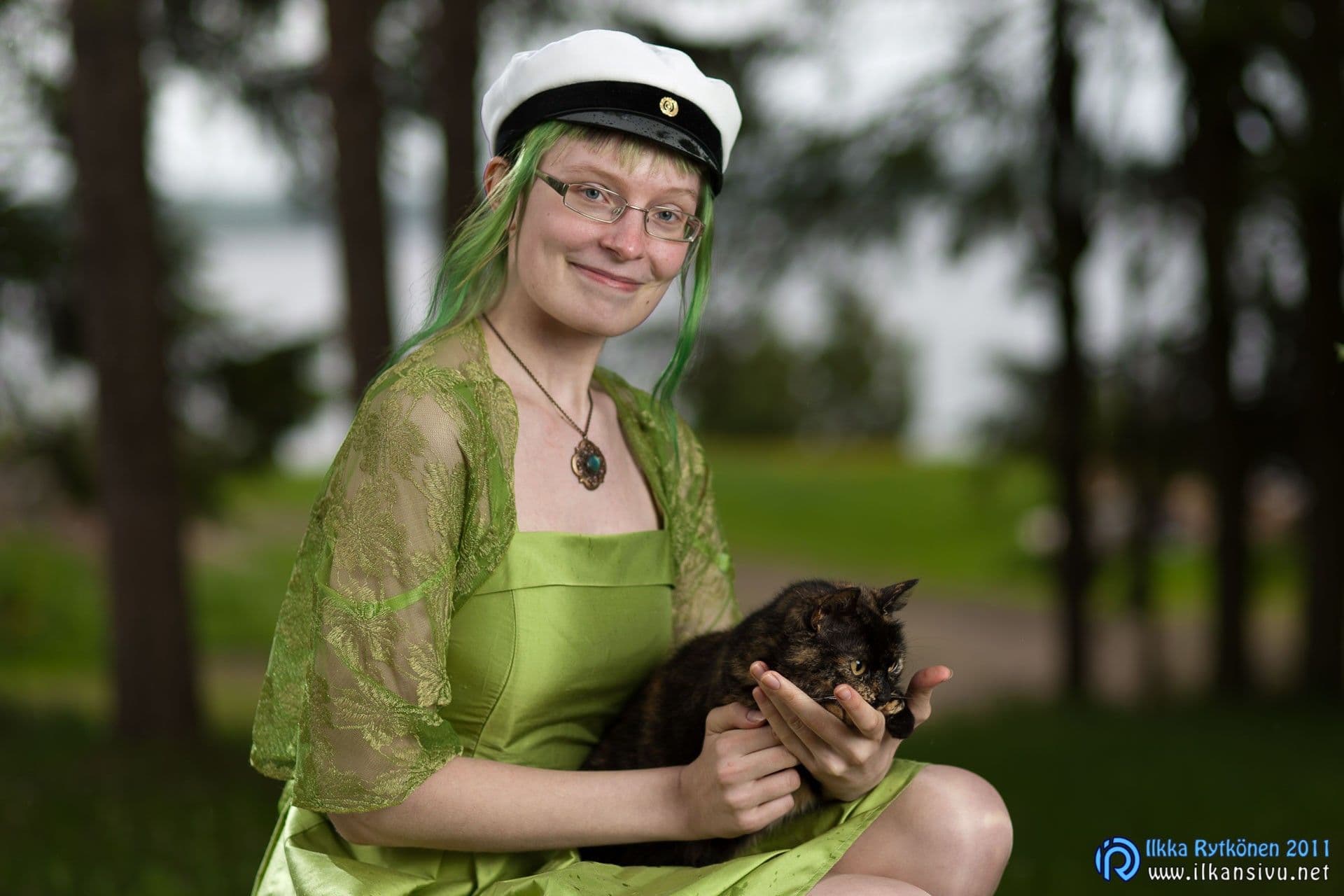 Vihreäpukuinen ylioppilas pitelee kilpikonnakuvioista kissaa ulkona