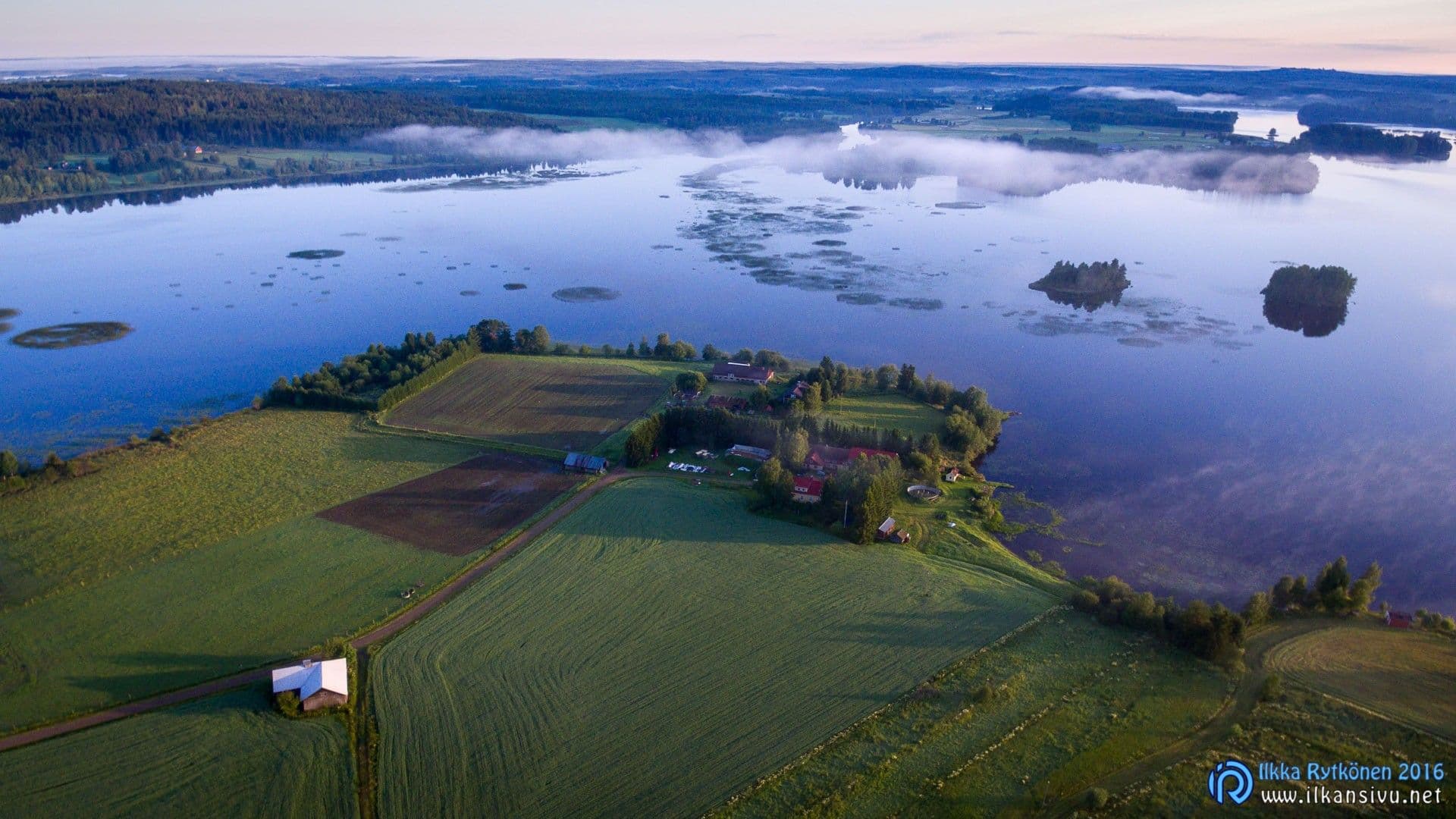 Aerial view of a lakeside farm surrounded by fields beside a calm lake