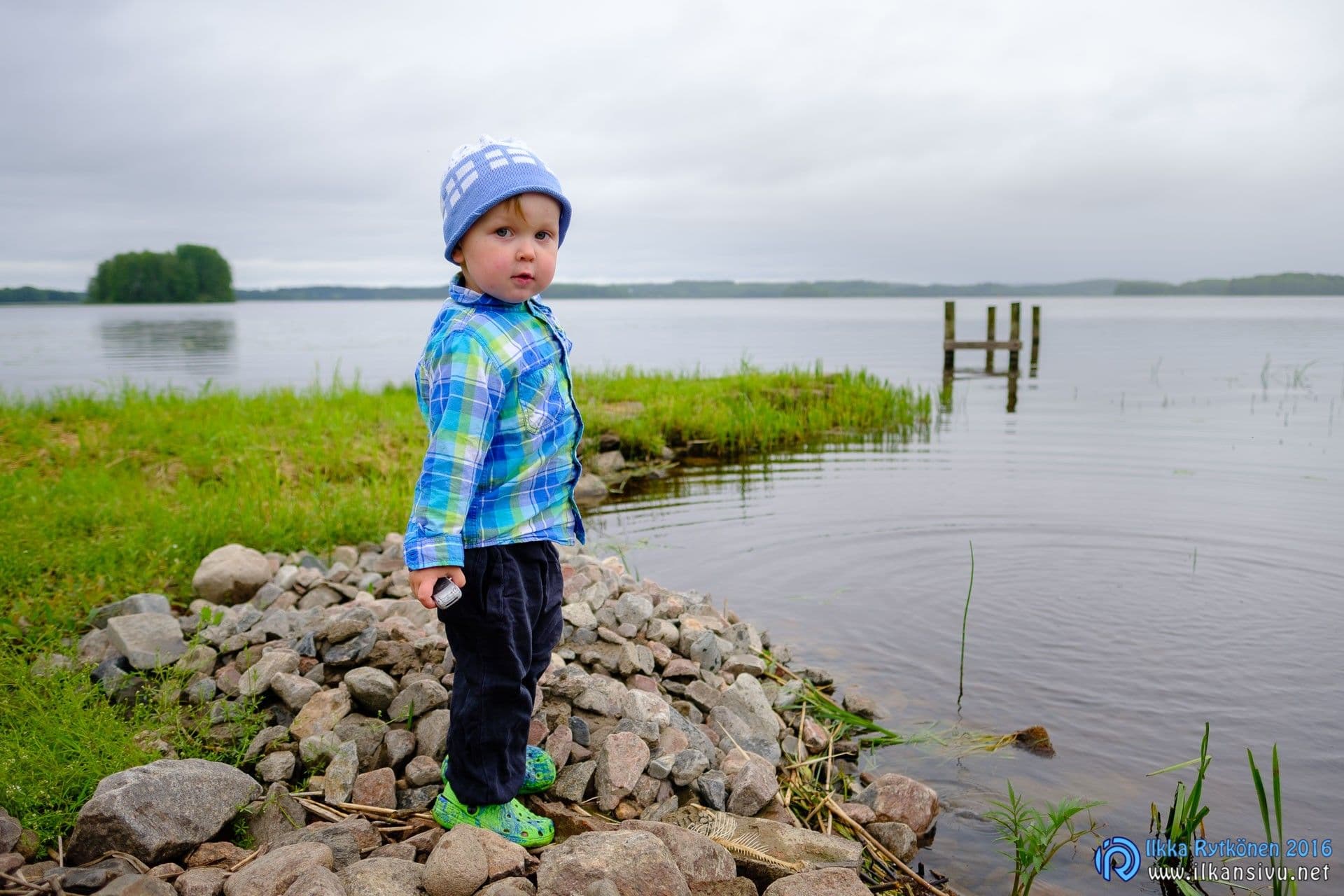 A child in a blue checked shirt stands on a rocky shore