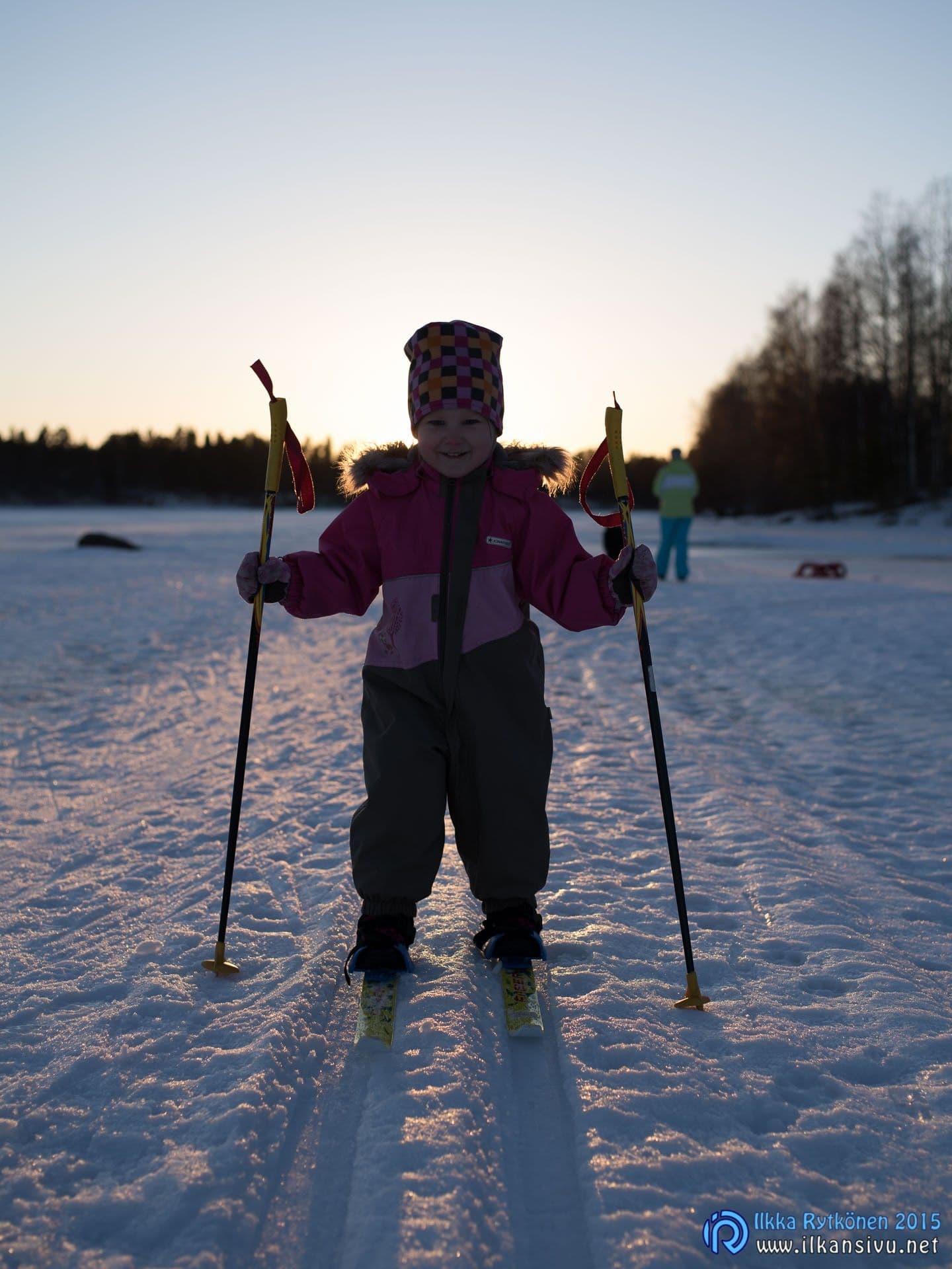 Lapsi seisoo suksilla lumessa vastavalossa, alkuperäisessä kuvassa kasvot jäävät varjoon