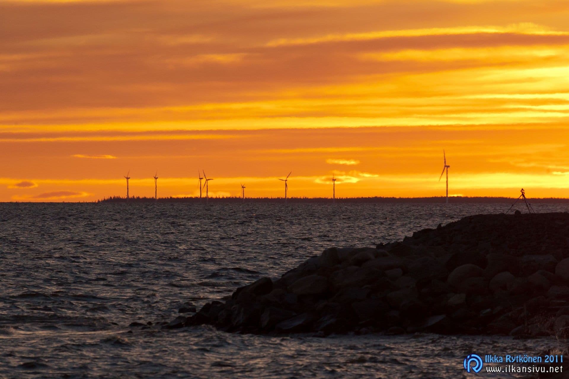Tuulivoimaloita meren horisontissa voimakkaan oranssissa auringonlaskussa