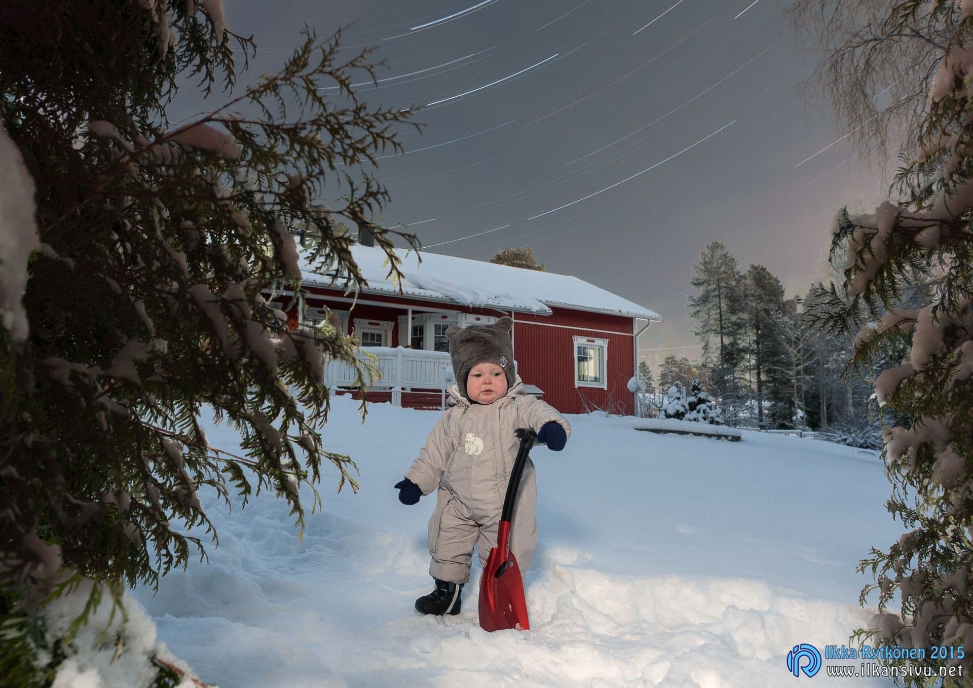 A child stands in a snowy yard beneath star trails