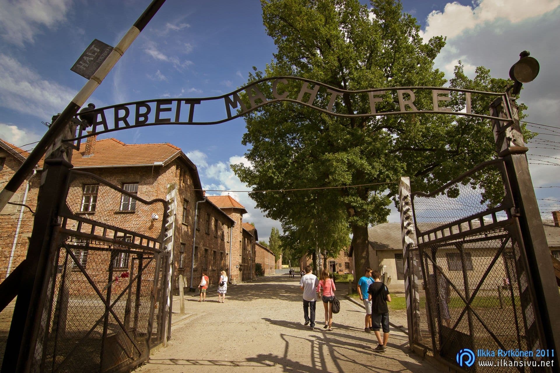 Auschwitz I:n sisäänkäynti Arbeit macht frei -kyltteineen ja vierailijoineen