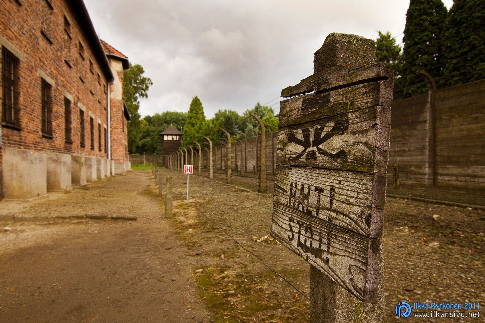 Halt Stój -kyltti piikkilanka-aidan ja vartiotornin vieressä Auschwitz I:ssä