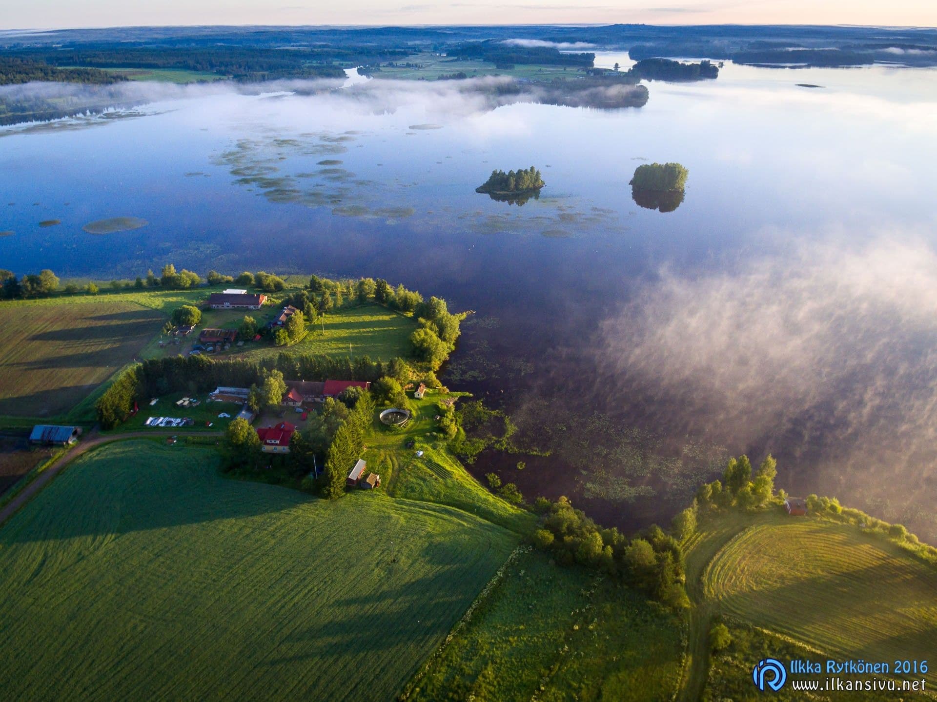 Aerial view of lakeside fields and mist drifting over the water